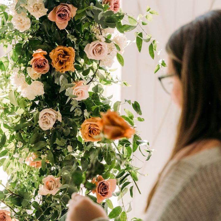 Frau vor einem Blumenbogen mit Rosen in verschiedenen Farben für eine Hochzeit.